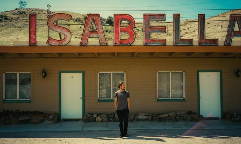 Man stands in front of Isabella motel with vintage sign under sunny sky