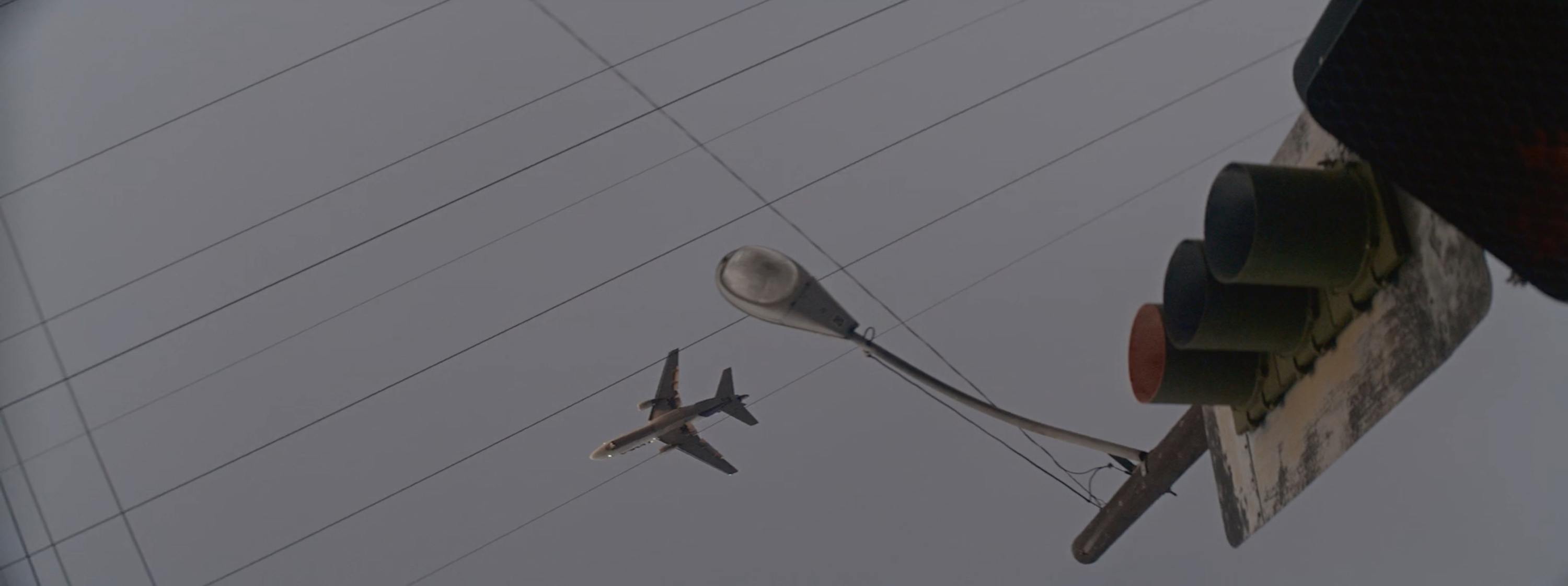 Aircraft flying low past streetlights and traffic signals against overcast sky