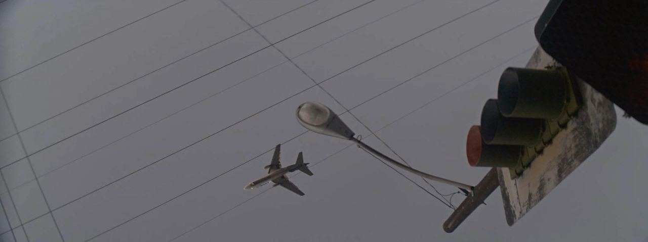 Aircraft flying low past streetlights and traffic signals against overcast sky