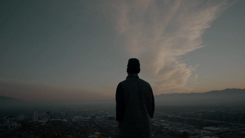Silhouette of a person overlooking a city at dusk with mountains in the distance