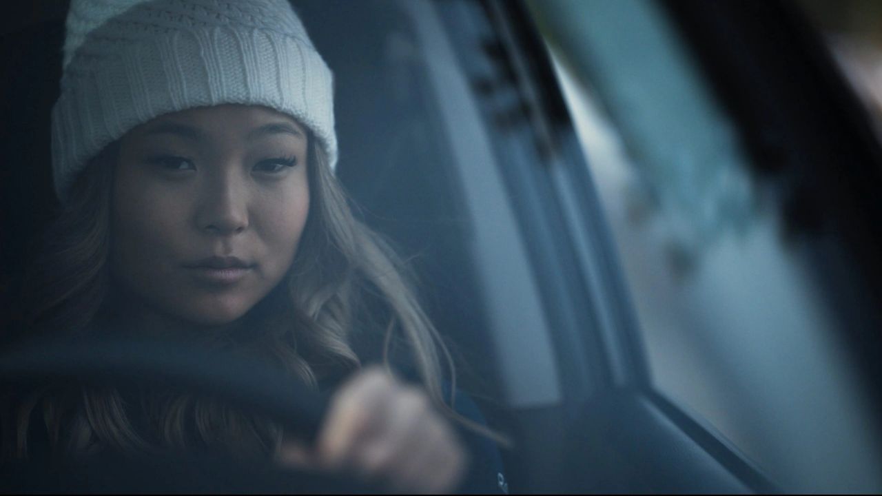 Olympic snowboarder Chloe Kim wearing a white beanie inside a car, hand on steering wheel.