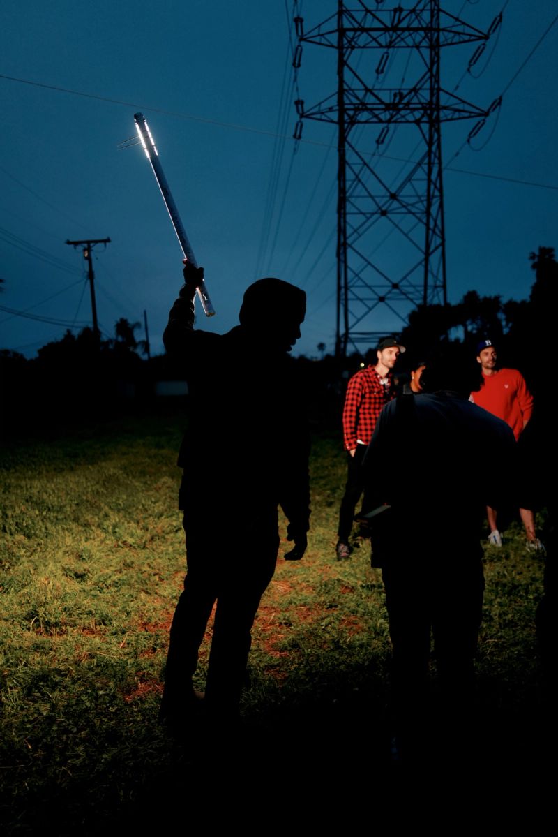 Silhouetted figures on grassy field at dusk with glowing light stick and power lines