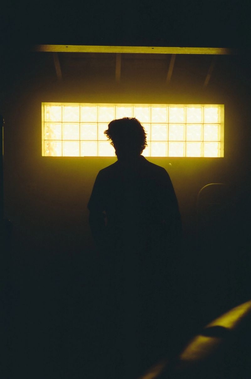 Cinematic silhouette of a figure backlit by a warm, glowing rectangular window of glass blocks.