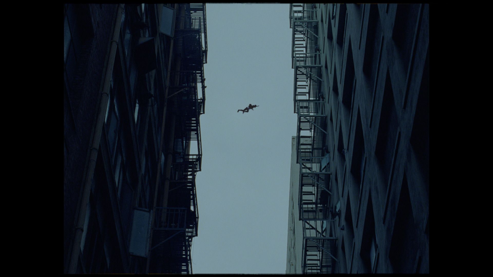 Silhouette of a person mid-air between two tall buildings under overcast sky