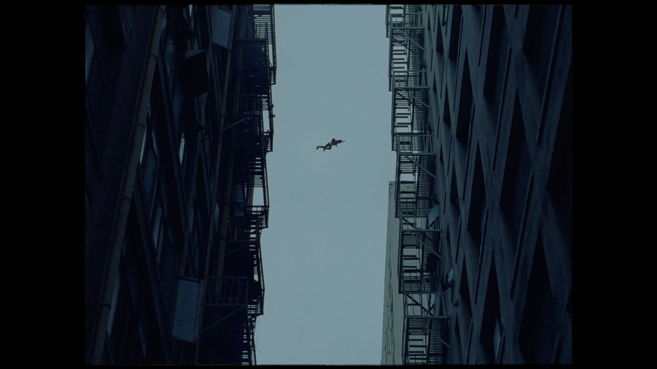 Silhouette of a person mid-air between two tall buildings under overcast sky