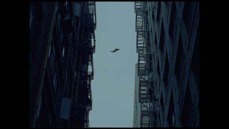 Silhouette of a person mid-air between two tall buildings under overcast sky