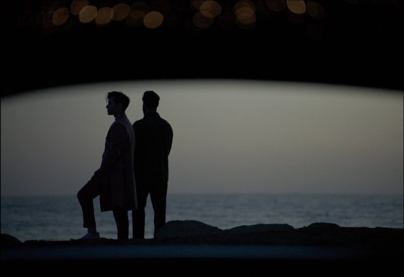Silhouetted men standing by the ocean at dusk, cinematic still from Rolls-Royce Inspiring Greatness.