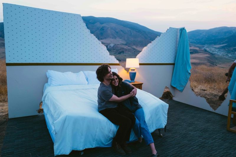 Couple embracing on a bed with broken wall overlooking mountain landscape at dusk