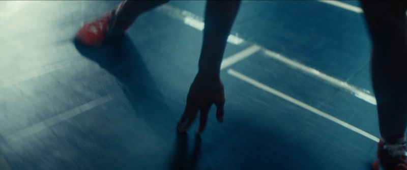 Close-up of Olympic wrestler Helen Maroulis in a low stance on a blue wrestling mat.
