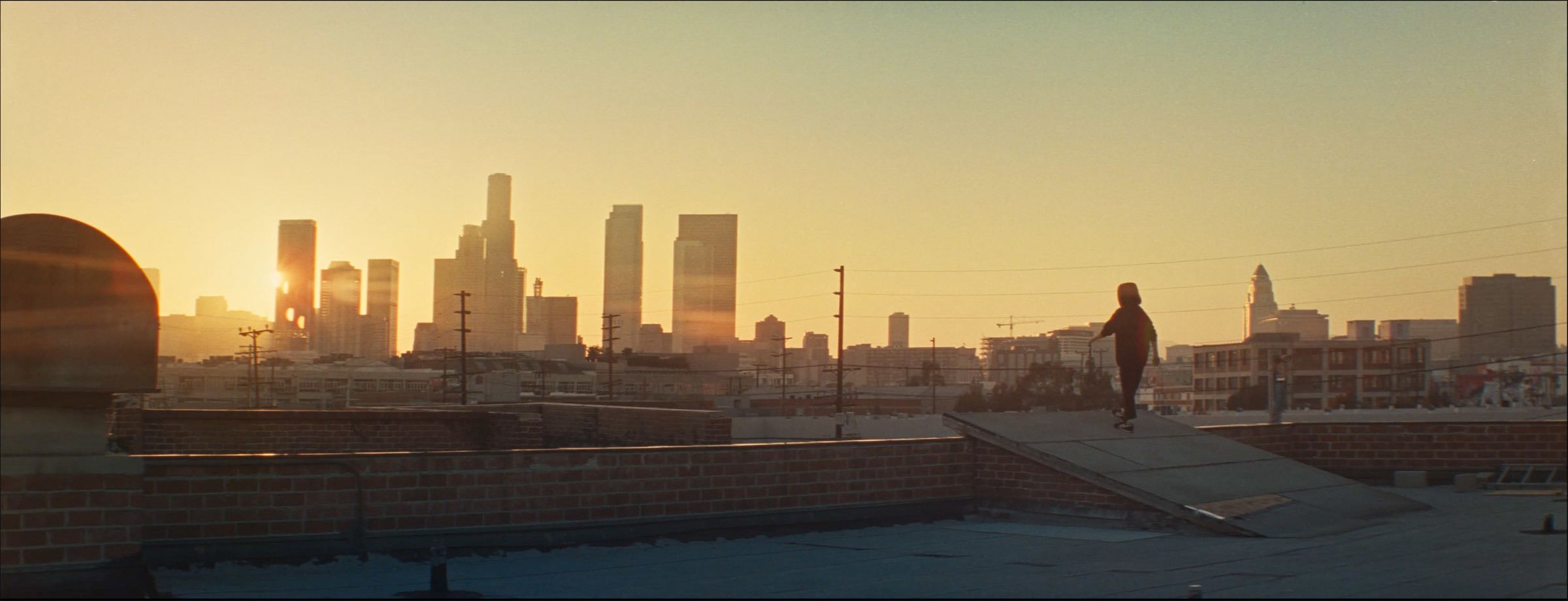 Skateboarder silhouetted against Los Angeles skyline at sunset on rooftop