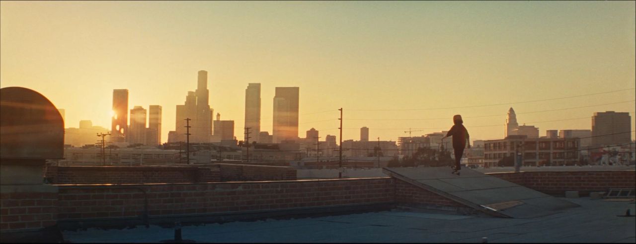 Skateboarder silhouetted against Los Angeles skyline at sunset on rooftop