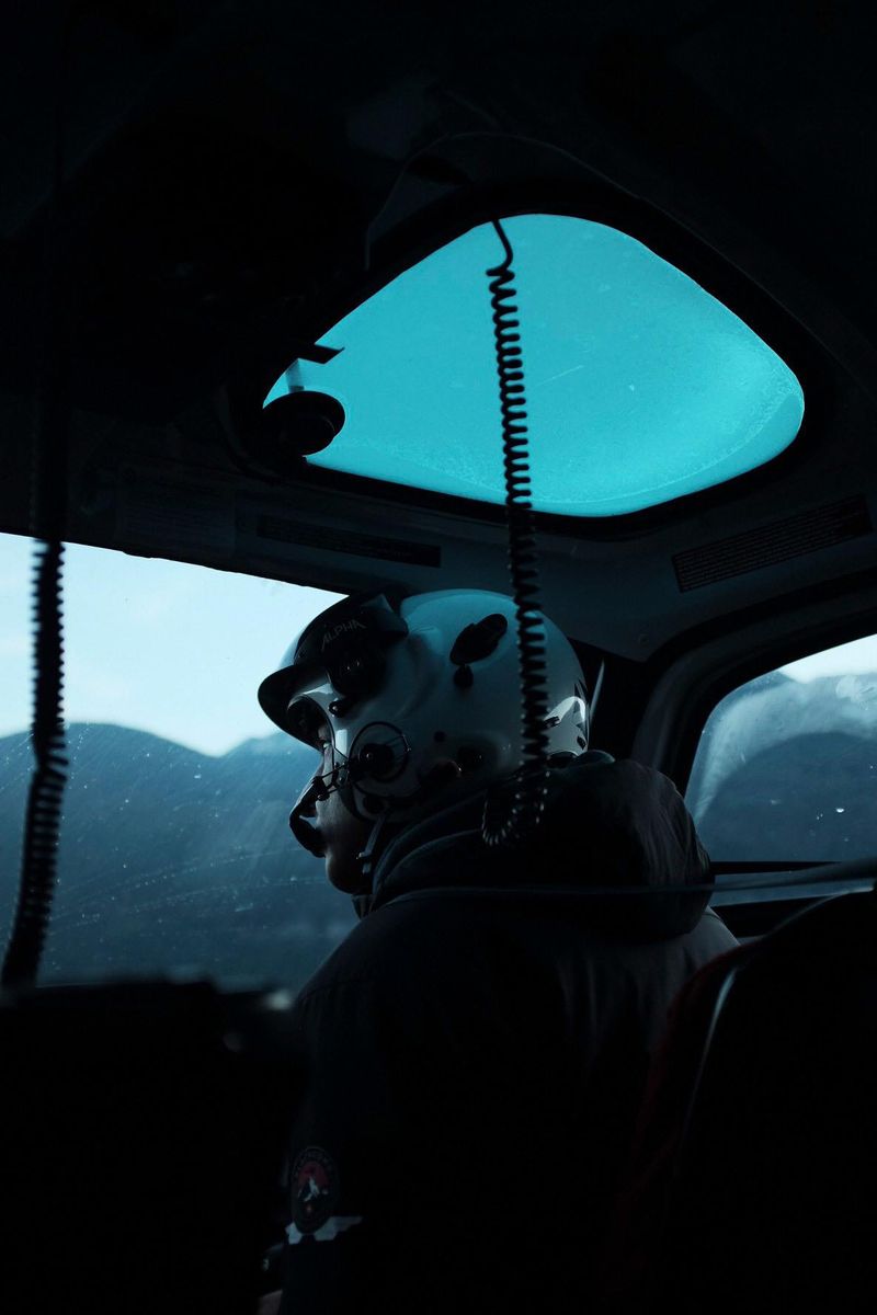 Cinematographer in helmet looking out helicopter window over snowy mountains