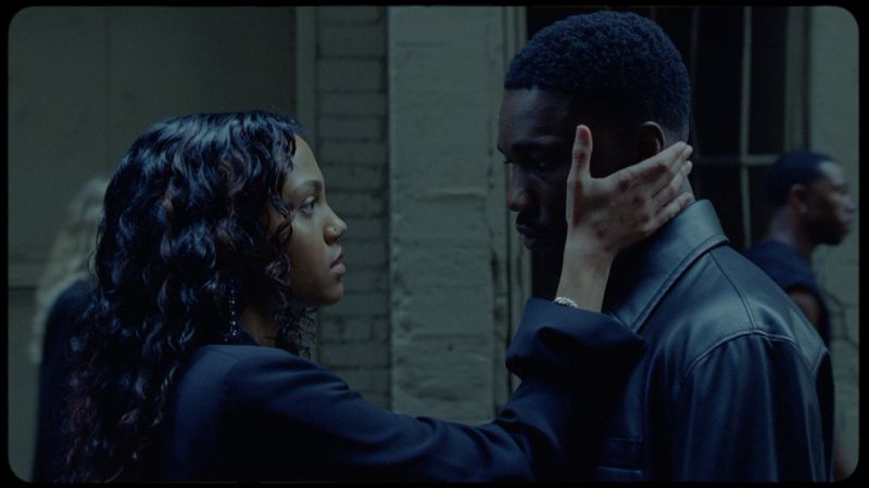 Woman gently holds man's face in dimly lit urban setting