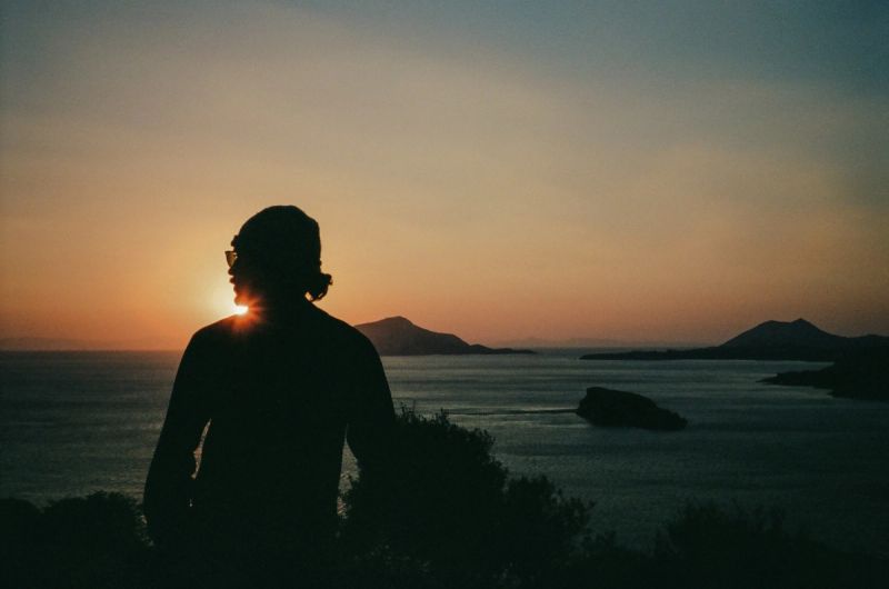 Silhouette of a cinematographer watching sunset over calm sea and islands.