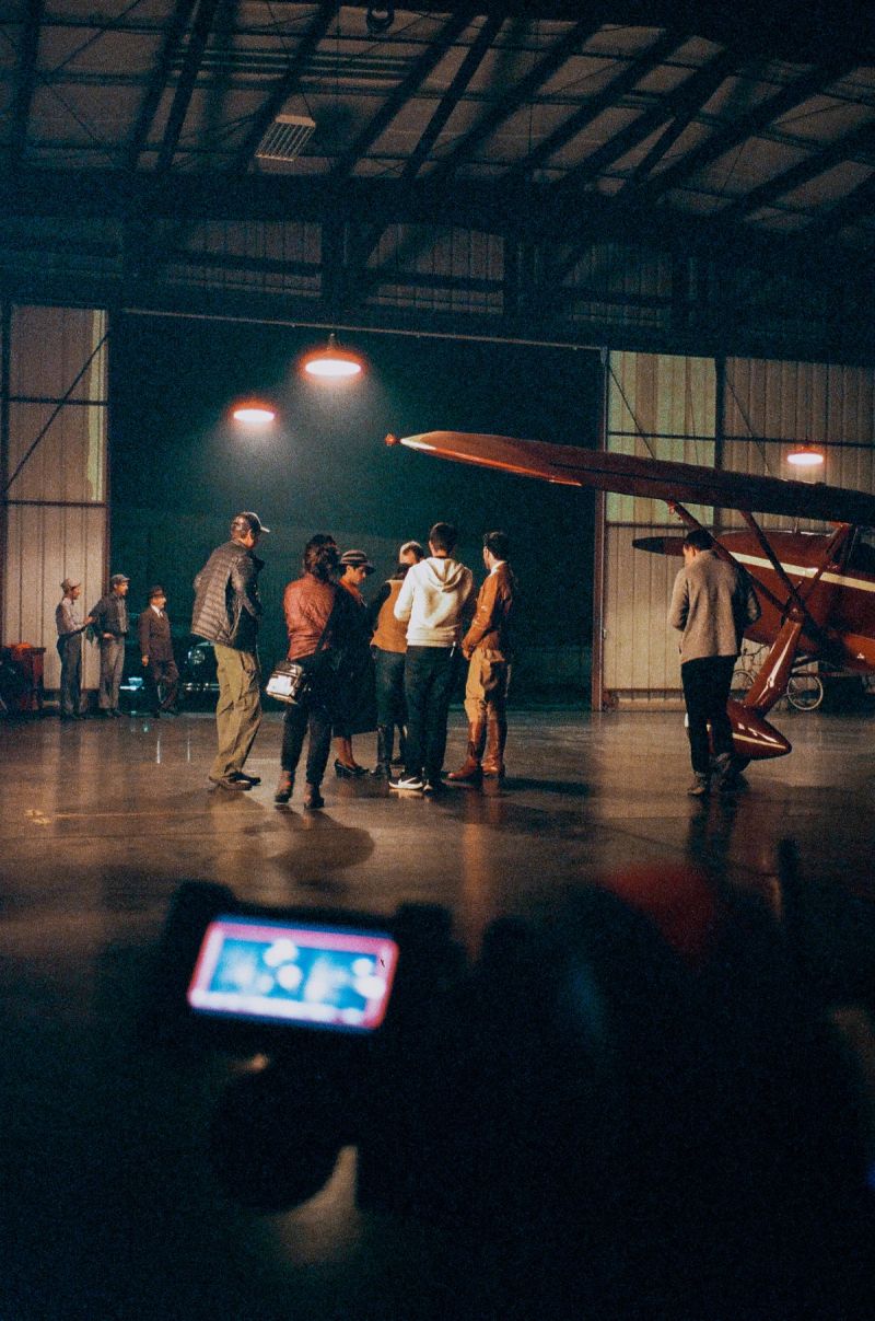 Group of people gathered around a vintage airplane in a dimly lit hangar, with film photography aesthetics.