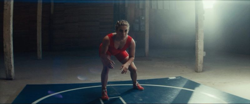 Olympic wrestler Helen Maroulis in a red singlet crouching on a blue mat with atmospheric backlighting.