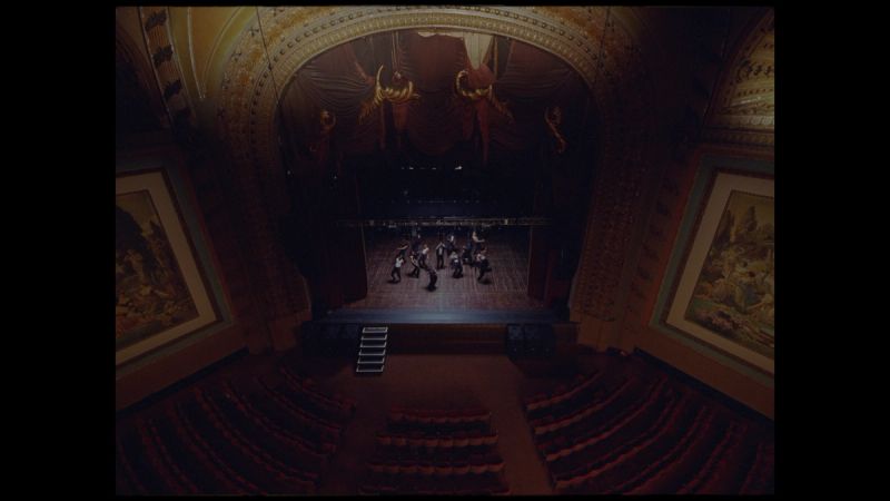 Orchestra performing on stage in ornate theater with red velvet seats