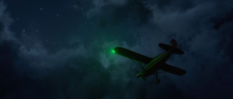 Green-lit airplane flying through cloudy night sky