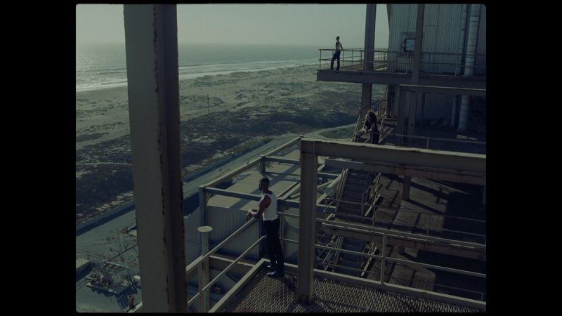 Three figures on industrial walkways overlooking coastal dunes and ocean
