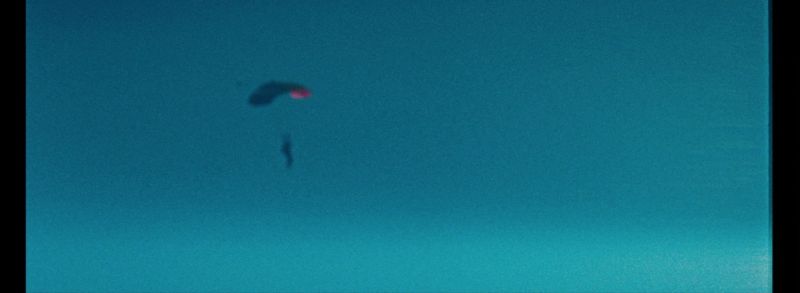 Skydiver freefalling with parachute against blue sky.