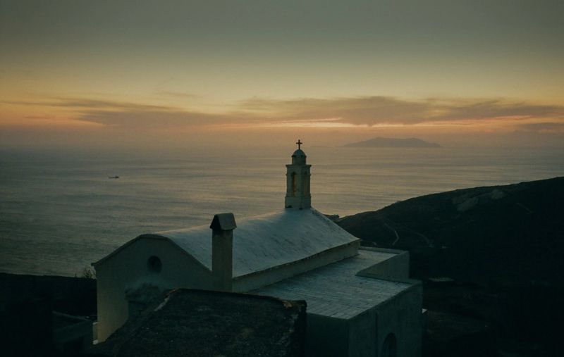 White church with bell tower overlooks the ocean at twilight.