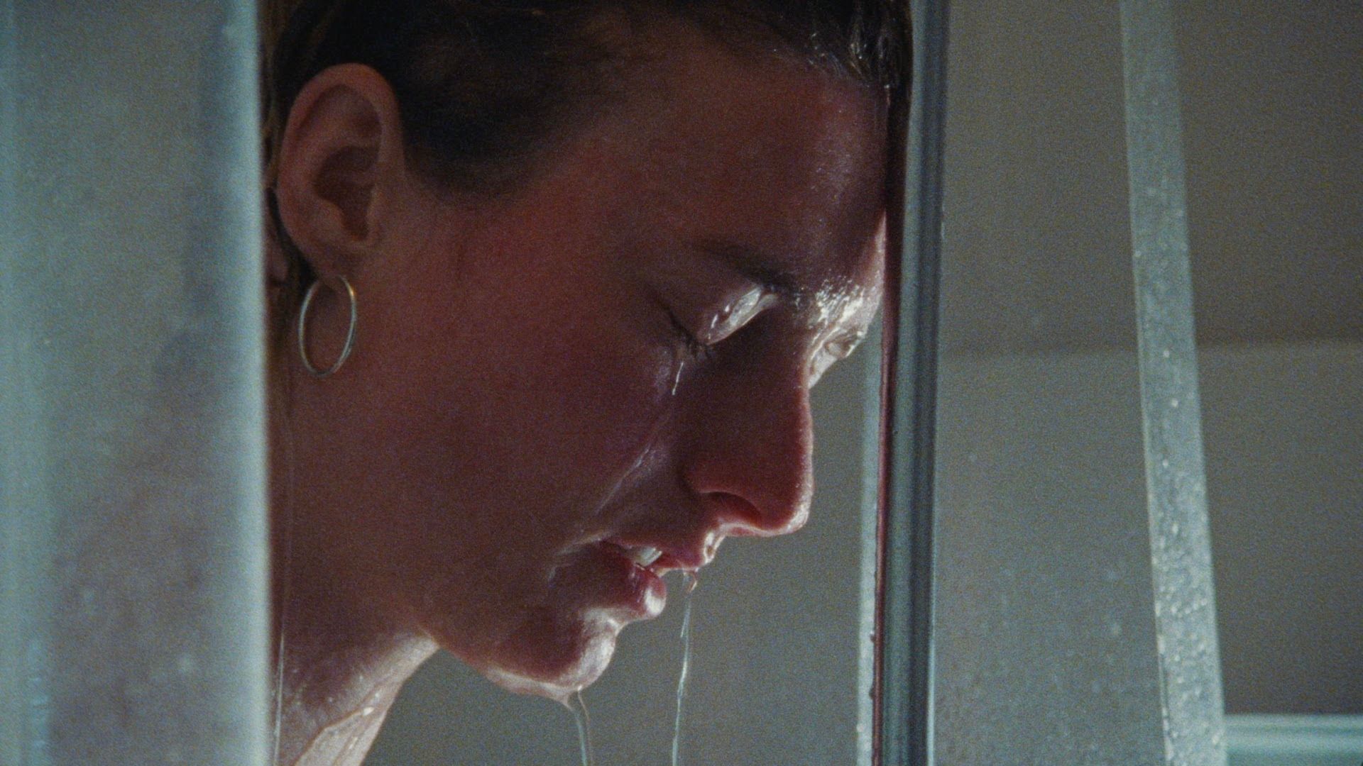 Close-up of a woman crying in a shower, water streaming down her face