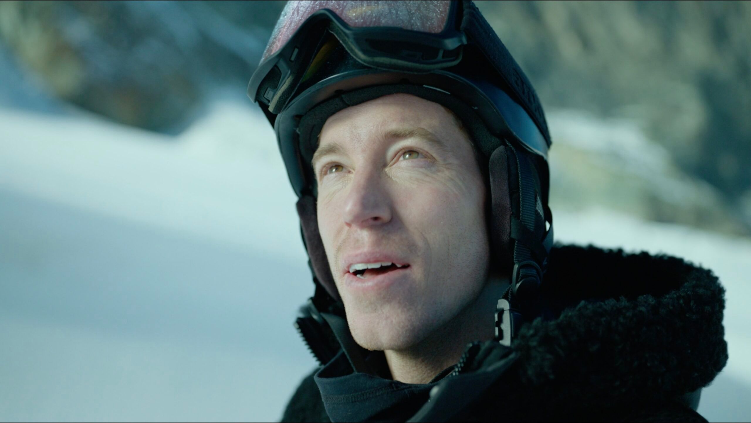 Shaun White in snowy mountain terrain wearing ski gear and helmet