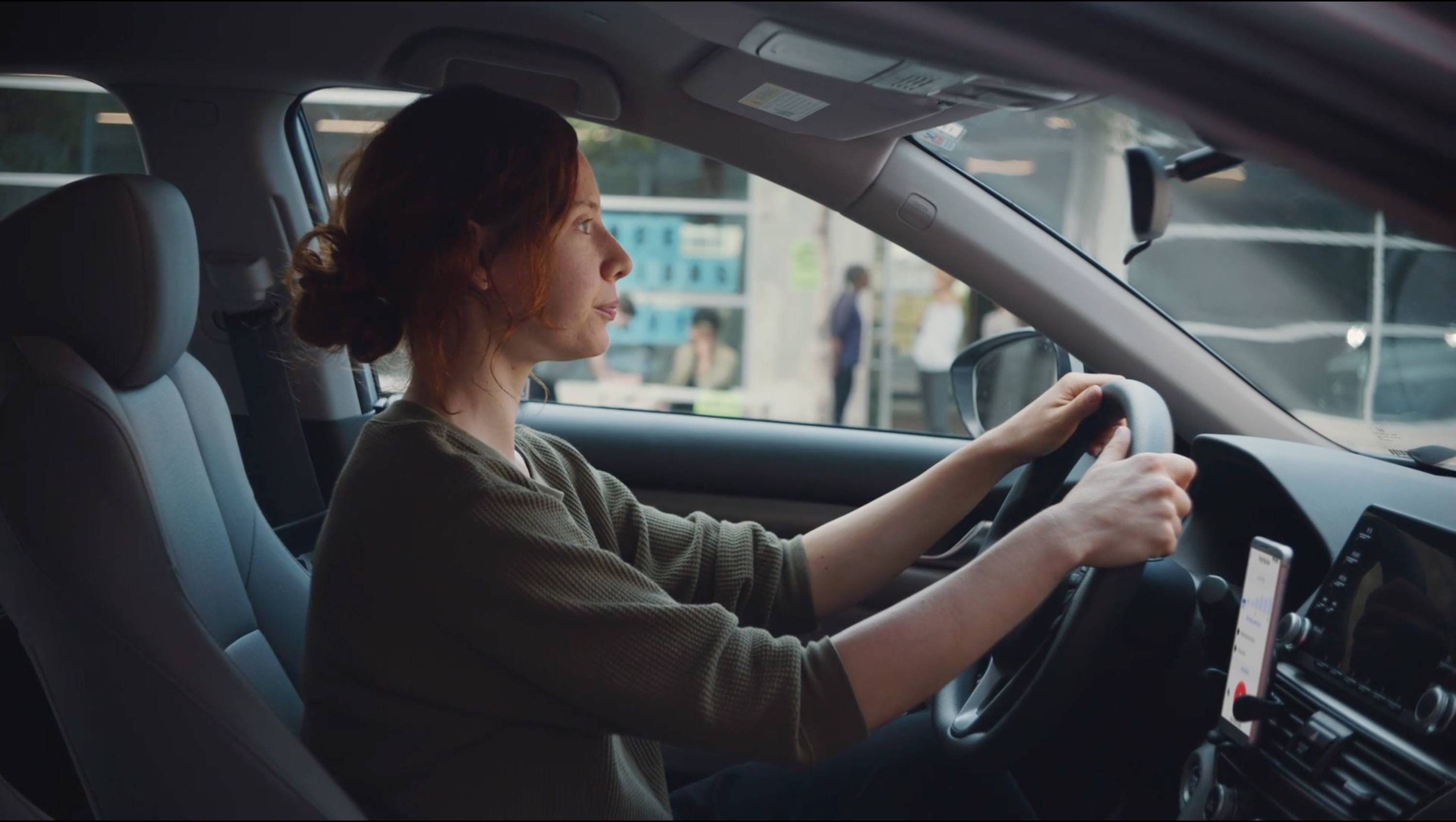 Side view of a woman driving a car with hands on the steering wheel.