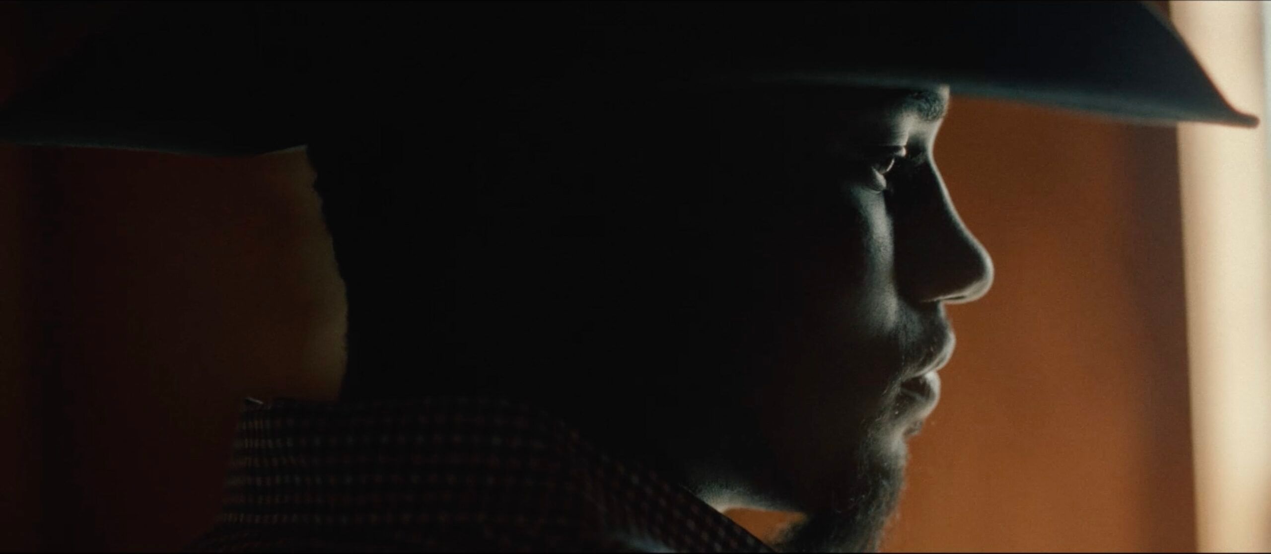 Profile of a man in cowboy hat and beard, side-lit with warm tones