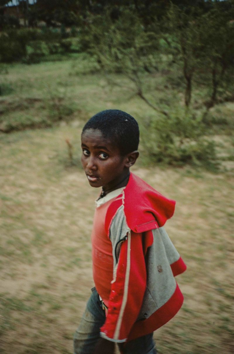 Young boy in red jacket looks back over shoulder outdoors.
