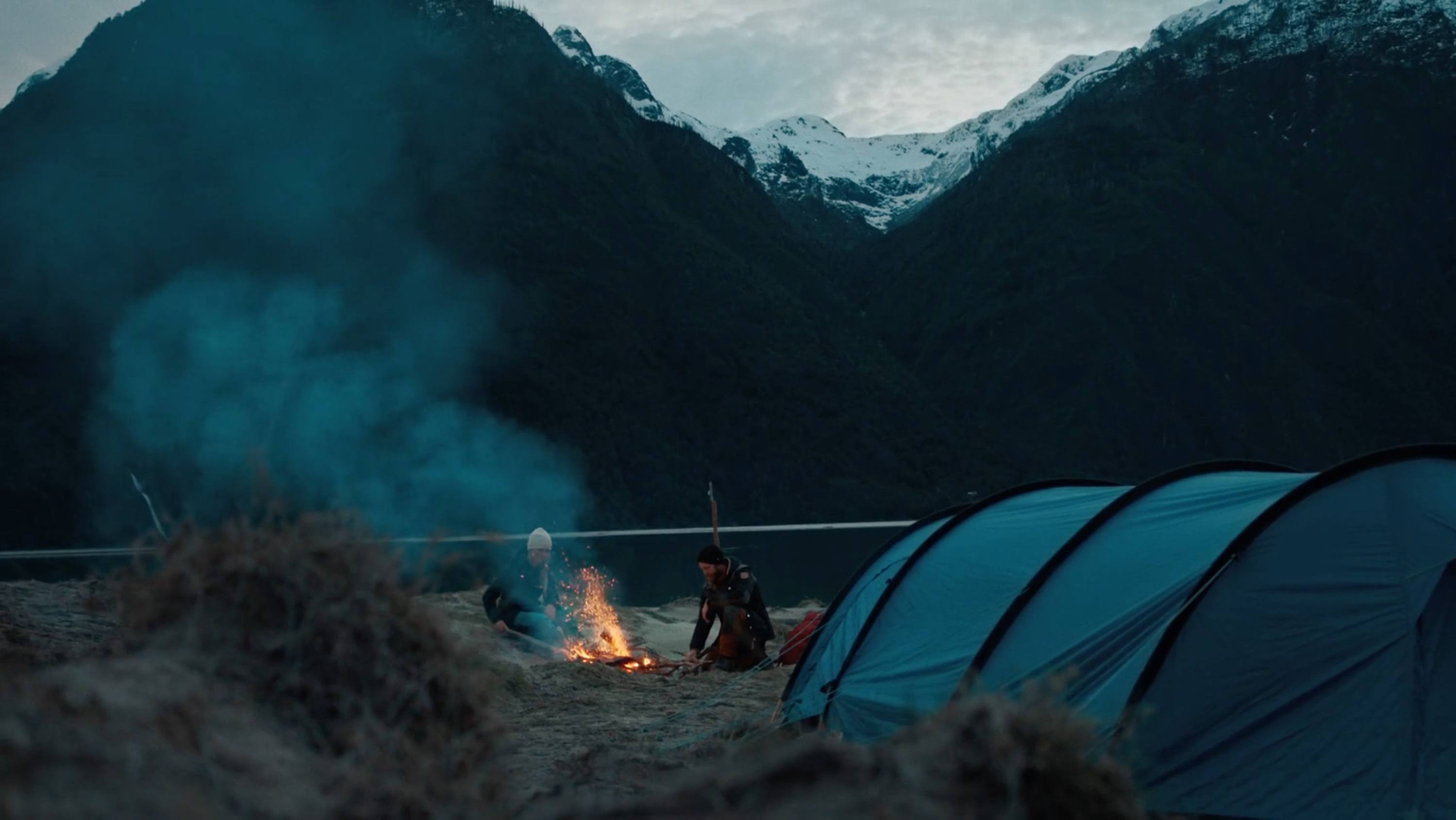 Campsite with blue tent and fire against dark mountains in Southern Patagonia.