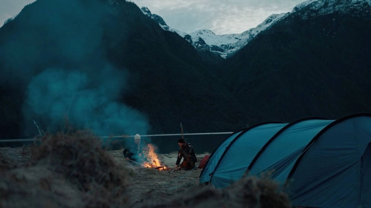 Campsite with blue tent and fire against dark mountains in Southern Patagonia.