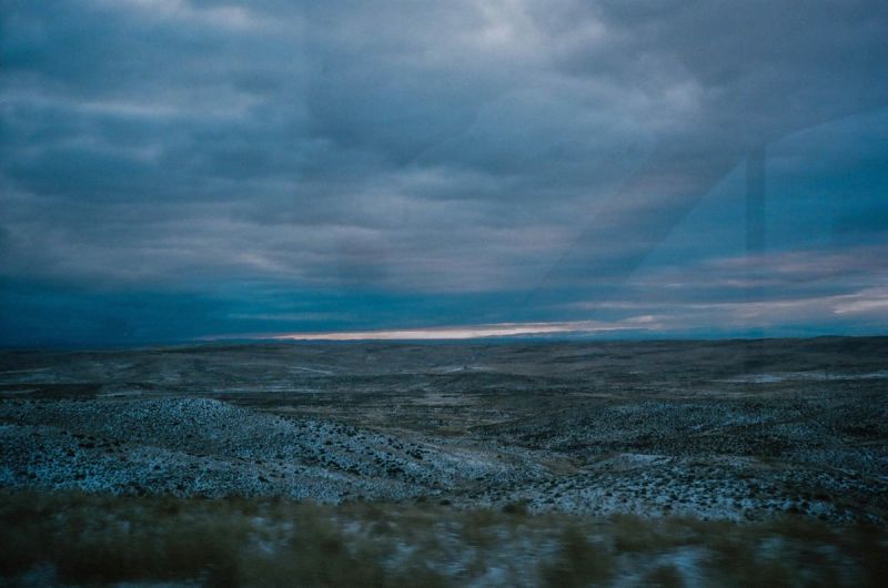 Dramatic overcast sky above rugged, snow-dusted desert landscape at dusk