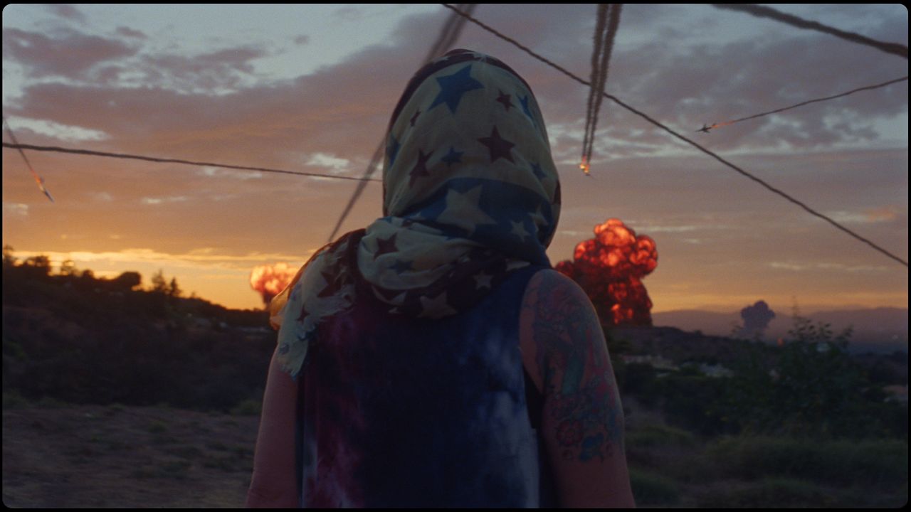 Person in star-patterned headscarf watches explosions at sunset