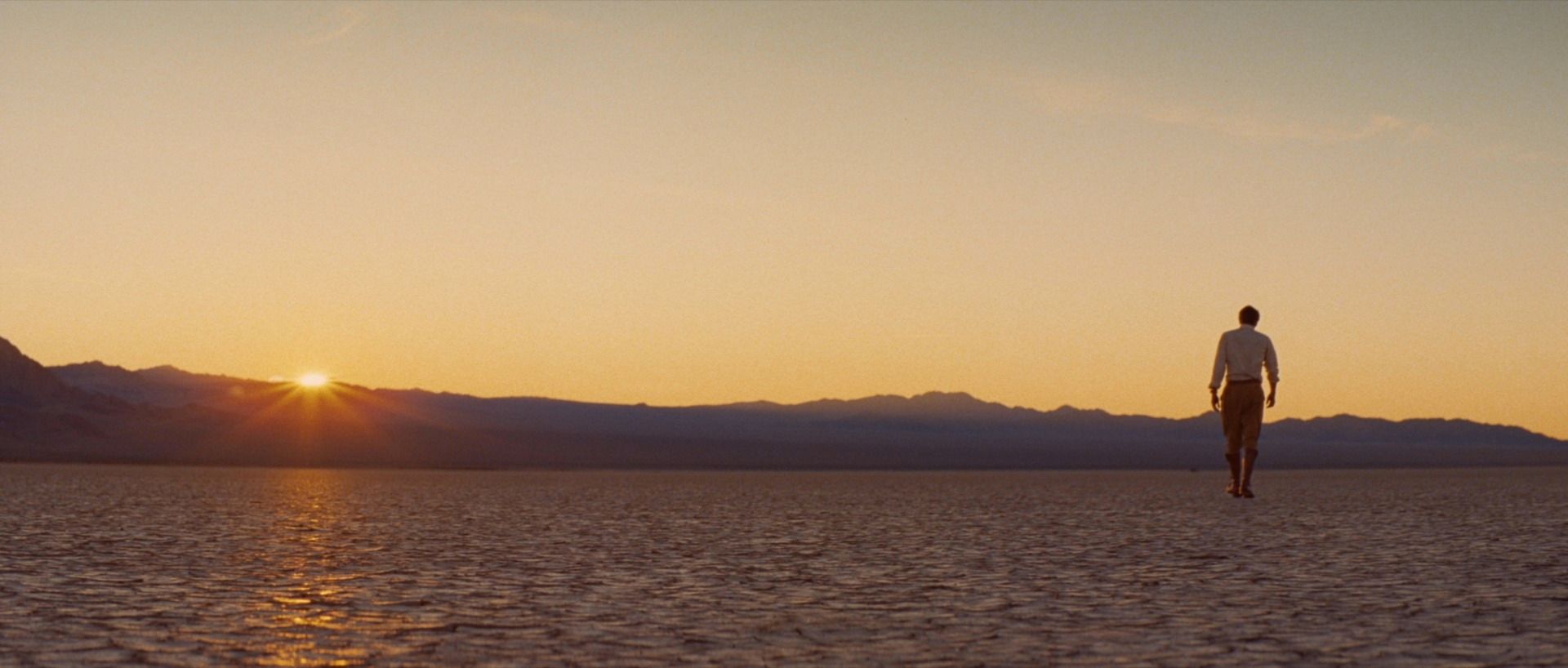 Man walking across salt flats at sunset with mountains in background