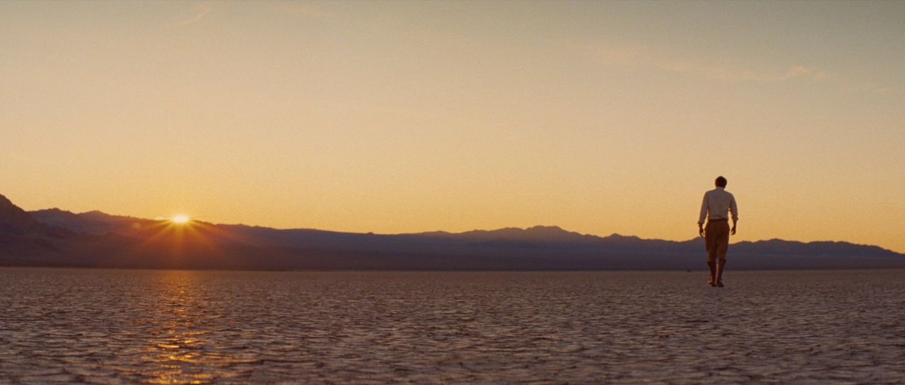 Man walking across salt flats at sunset with mountains in background