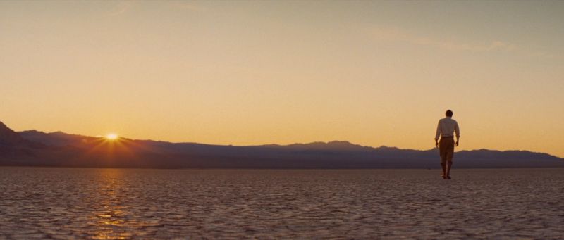 Man walking across salt flats at sunset with mountains in background