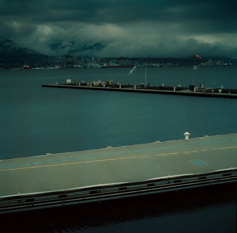 Cinematographer Ian Rigby captures moody waterfront scene with city skyline and mountains under stormy sky