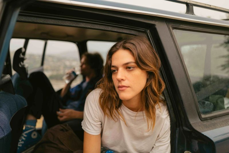 Woman with wavy brown hair looking out of a vintage car window
