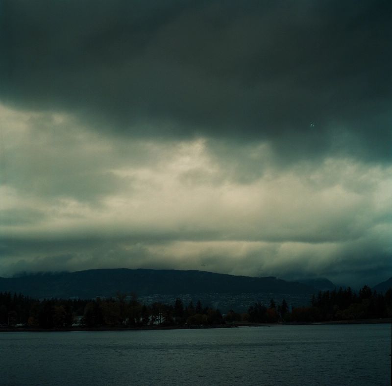 Dark storm clouds loom over a mountain range and lake shoreline.