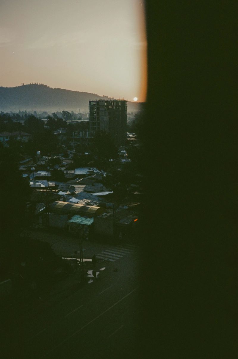 A hazy sunset over an Ethiopian town with rooftops and a construction site near hills.