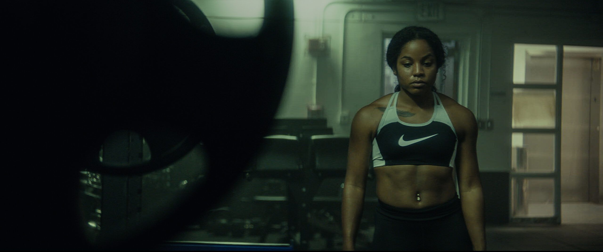 Jen Welter in Nike sports bra stands focused in a dimly lit industrial space for the EastBay ConqHer Santia Deck shoot.