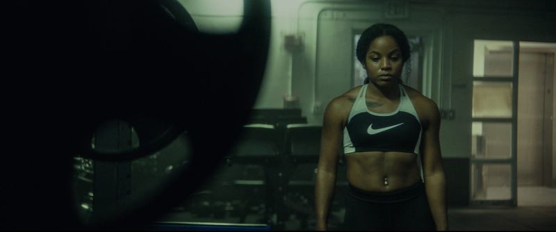 Jen Welter in Nike sports bra stands focused in a dimly lit industrial space for the EastBay ConqHer Santia Deck shoot.