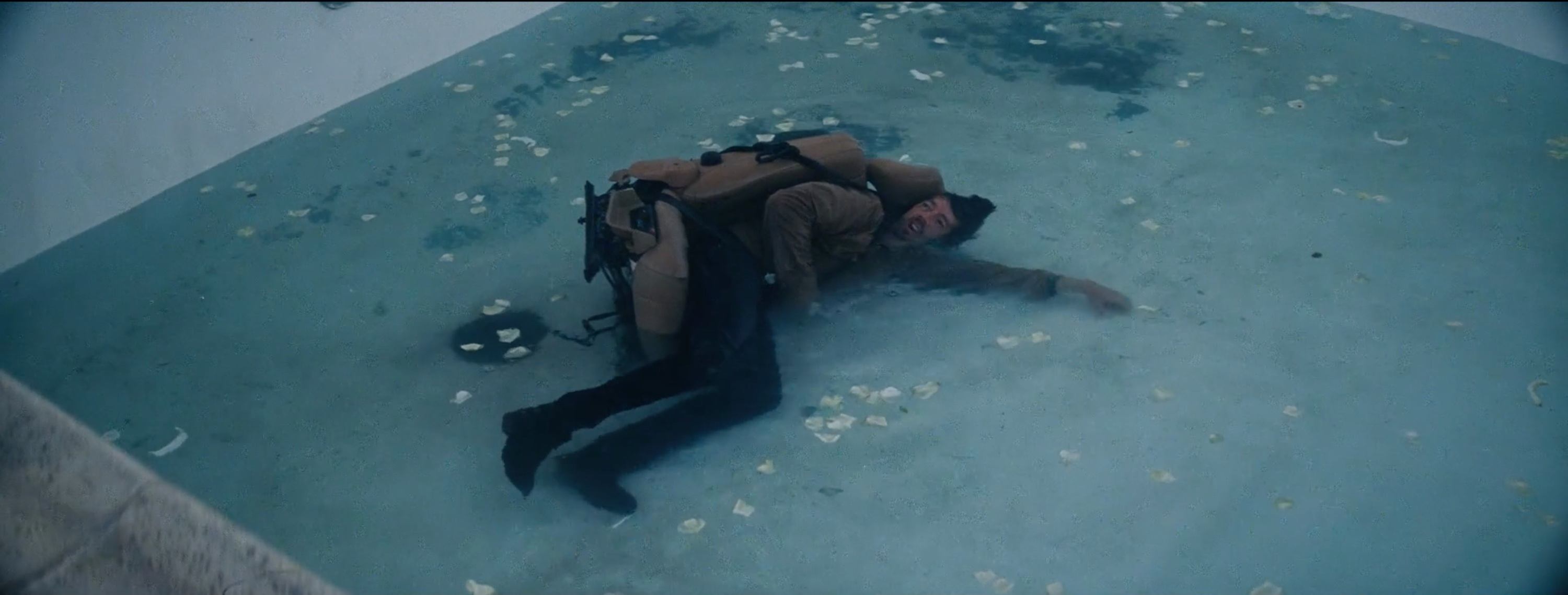 Actor in brown jacket and black pants lying on wet concrete with scattered white petals