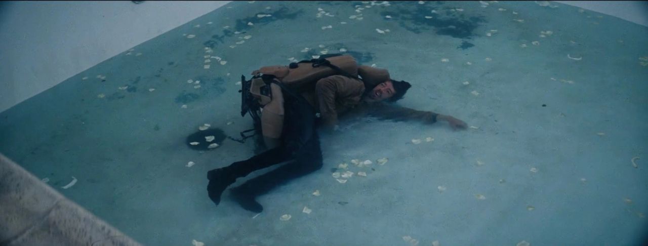Actor in brown jacket and black pants lying on wet concrete with scattered white petals