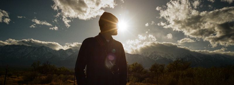 Silhouette of a figure against bright sun and snow-capped mountains during Toyota Olympics production.