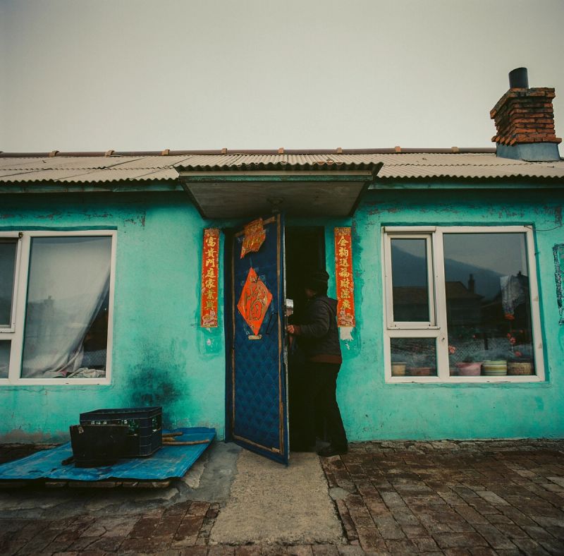 Person entering turquoise house with red Chinese couplets and blue door