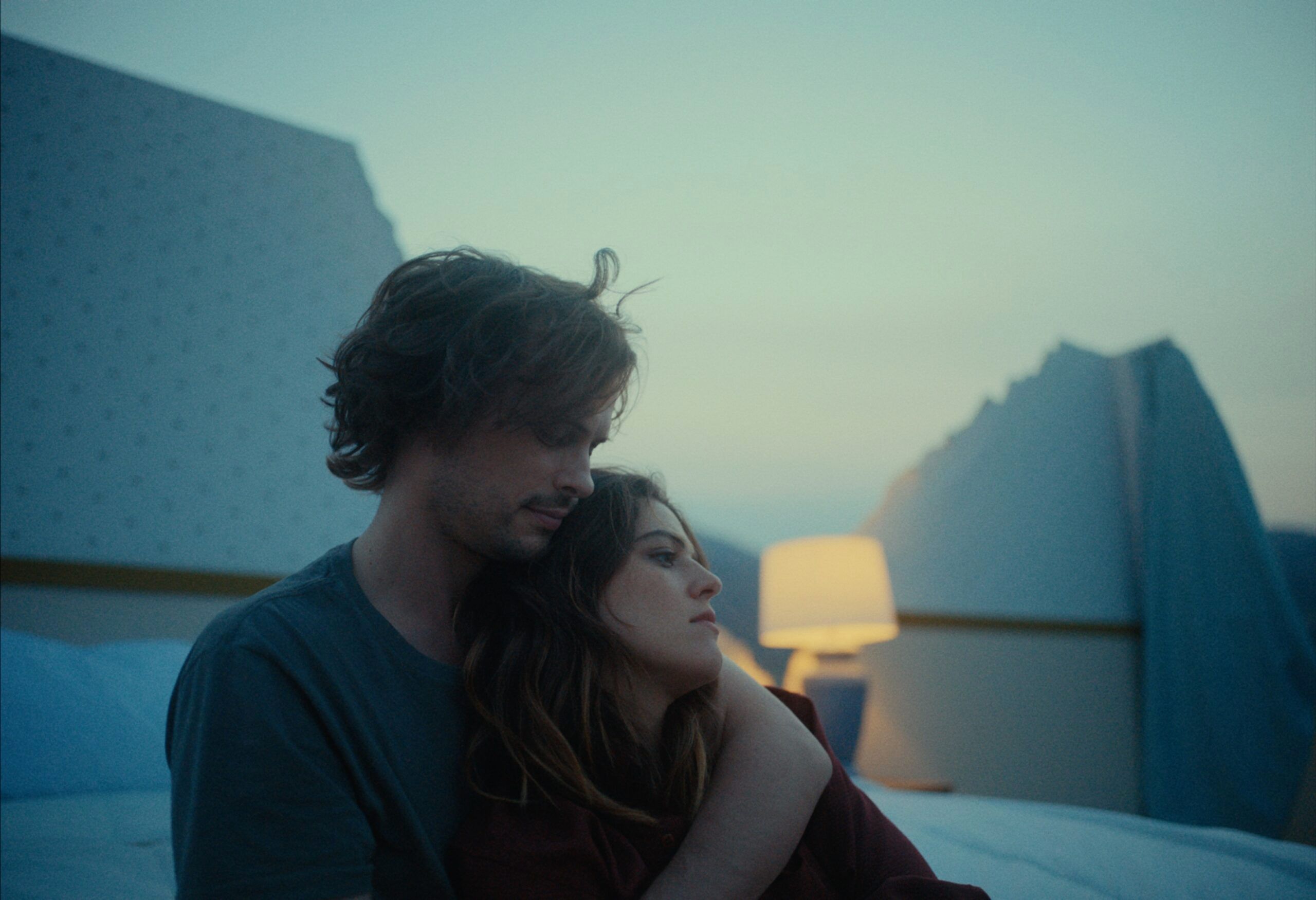 Couple embracing on a bed with mountain backdrop at dusk