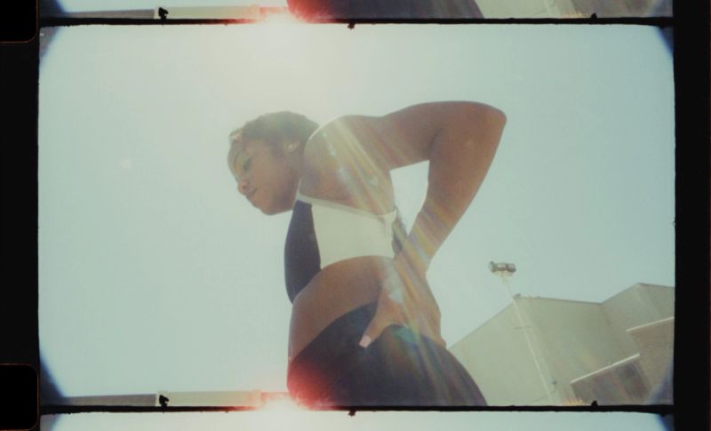 Low angle film portrait of female athlete stretching with intense sun flare and lens bloom.