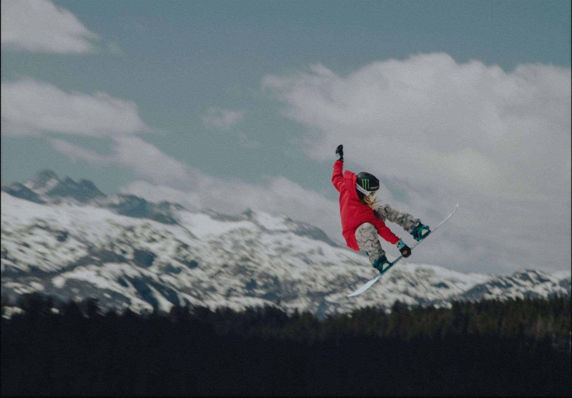 Snowboarder in red jacket mid-air against snowy mountains